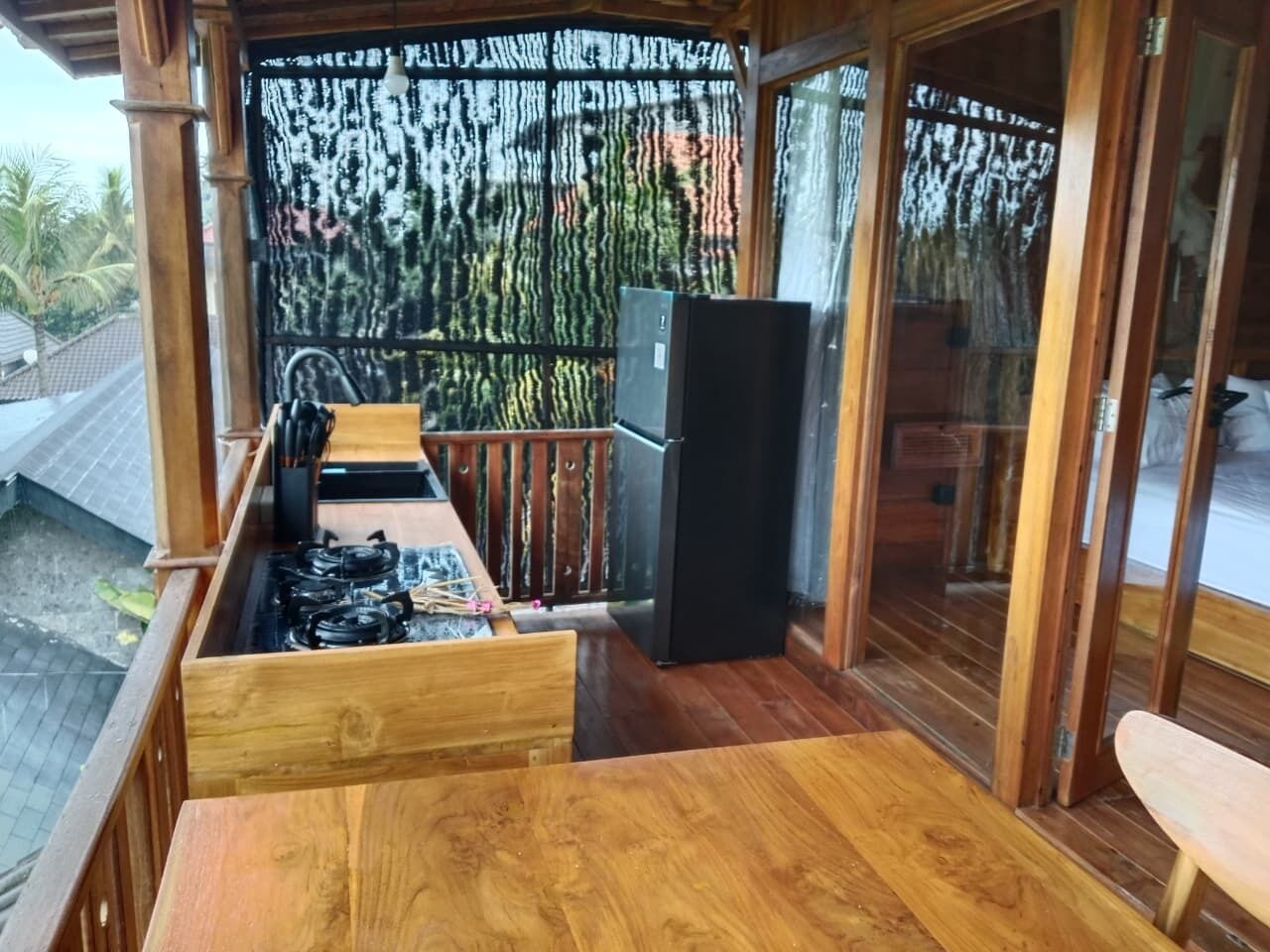 A wooden deck with a gas stove, a refrigerator, and a sliding glass door leading to a balcony.