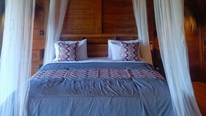 A wooden four-poster bed with a canopy, a patterned bedspread, and pillows. - Rana Suite (Ubud)