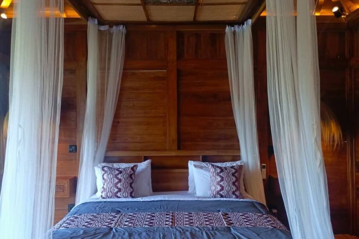 A wooden four-poster bed with a canopy, a patterned bedspread, and pillows.