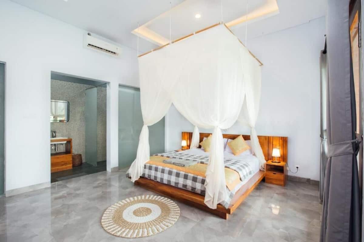 A bedroom with a four-poster bed, a bedside table with a lamp, and a round woven rug.