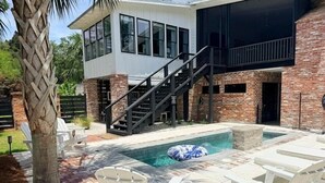 Una casa moderna con piscina, mobiliario exterior y una escalera que conduce al nivel superior.