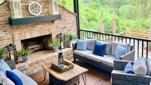 Un espacio de estar al aire libre cubierto con mobiliario de mimbre, chimenea y vistas a la vegetación.
