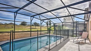 A covered swimming pool with a metal frame, a patio area with chairs, and a view of the surrounding landscape. - 5BR Home near Disney w/ Arcade & Private Pool (Davenport)