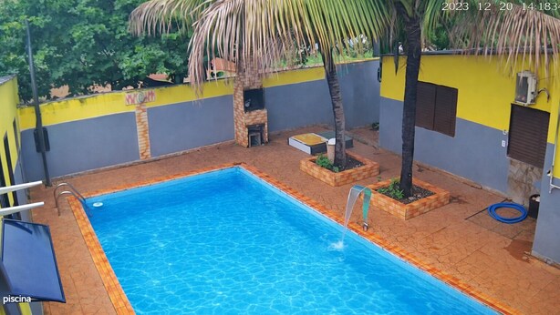 Una piscina rectangular con superficie de agua azul cristalina, rodeada por una terraza con suelo de baldosas formando un diseño de ladrillo.