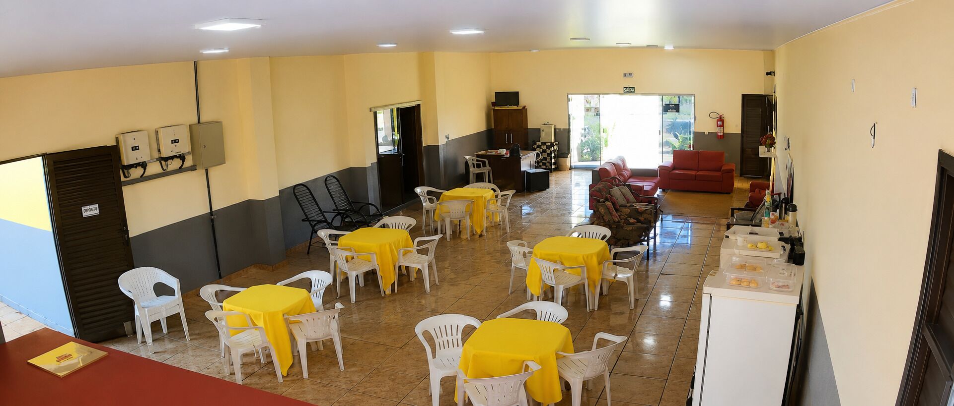 A dining area with multiple tables and chairs, a kitchenette, and a red sofa.
