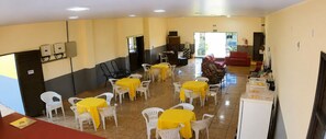 A dining area with multiple tables and chairs, a kitchenette, and a red sofa. - Hotel Recanto do Sol 1 (Alto Taquari)