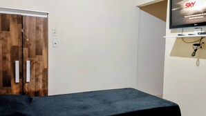 Una habitación con puerta de madera, televisor de pantalla plana montado en la pared y cama con cubierta oscura.