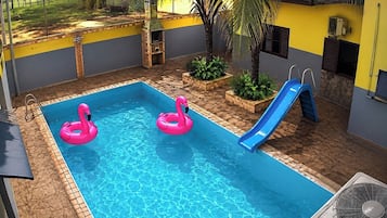 Una piscina con dos aros inflables rosados y un tobogán azul.