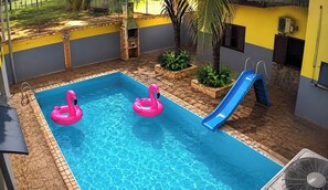 A swimming pool with two pink inflatable rings and a blue slide. - Hotel Recanto do Sol 1 (Alto Taquari)