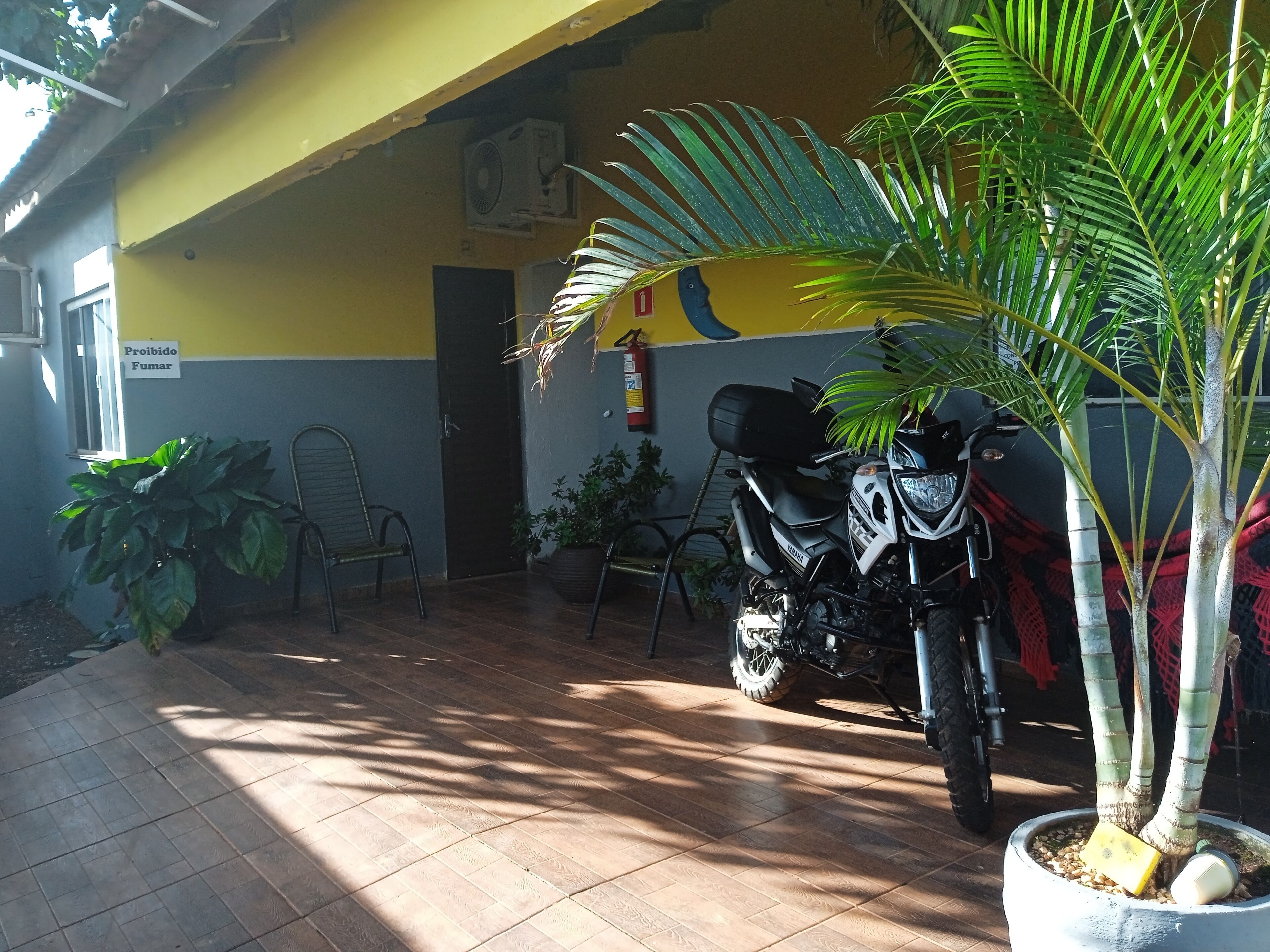 Uma motocicleta estacionada dentro de um edifício com piso de azulejos, parede amarela e uma placa com a inscrição 'Prohibido Fumar'.