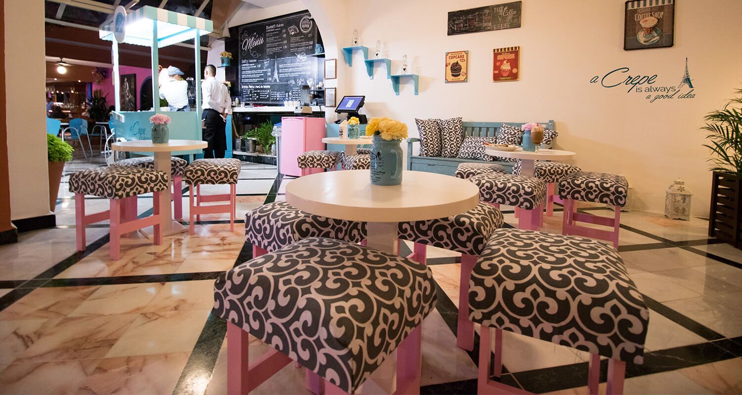 Un café avec des tables rondes et des chaises à motifs, un tableau affichant le menu et un mur décoré sur le thème des cafés.
