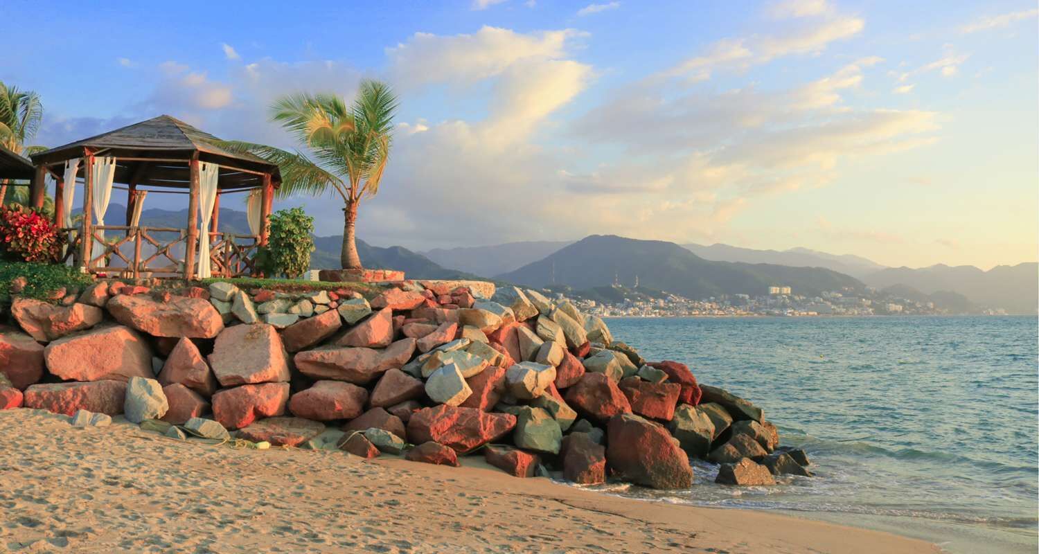 A beach with a gazebo, palm trees, and a rocky shoreline.