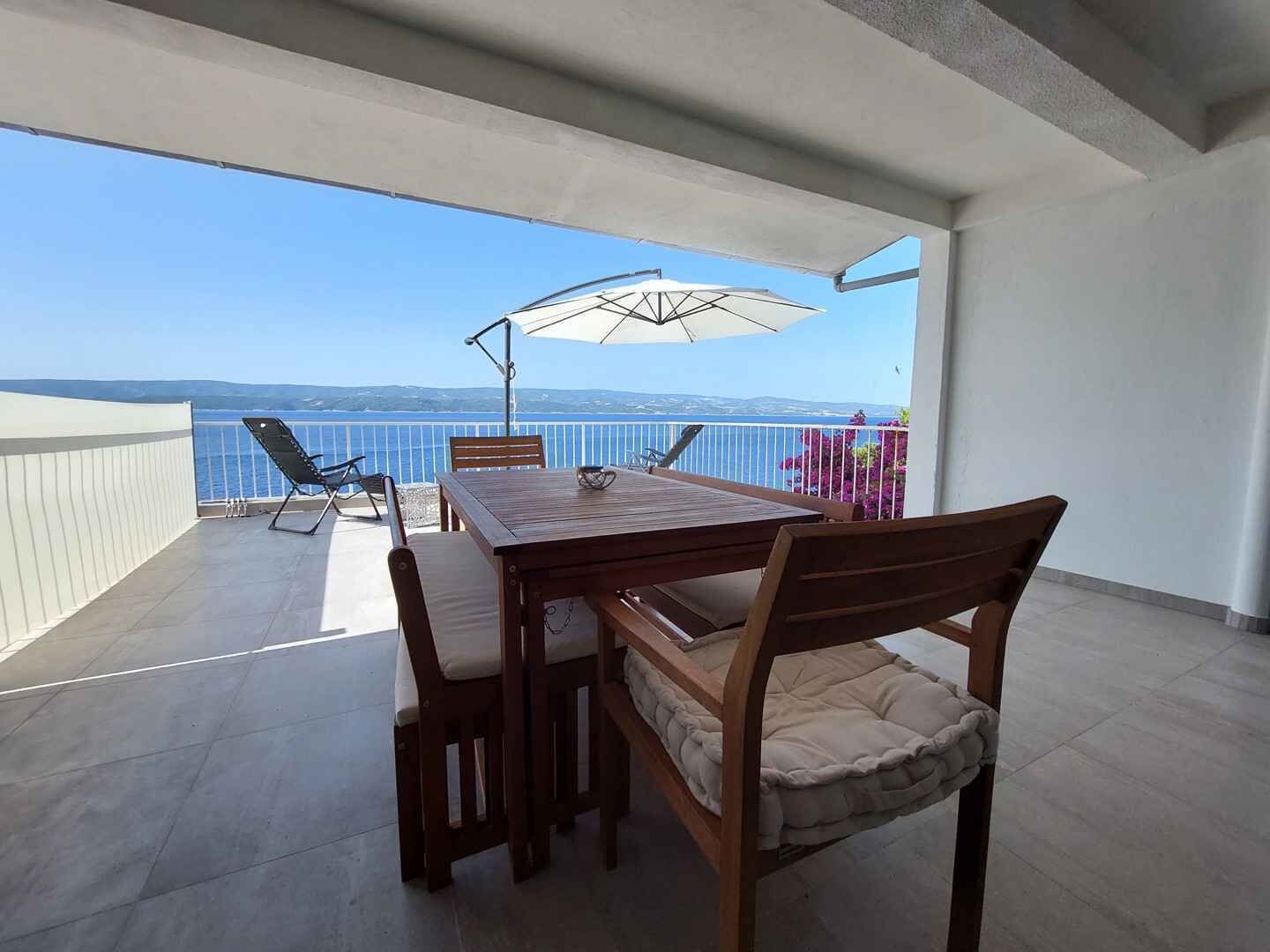 Un balcon avec une table et des chaises en bois, un parasol et une vue sur la mer.