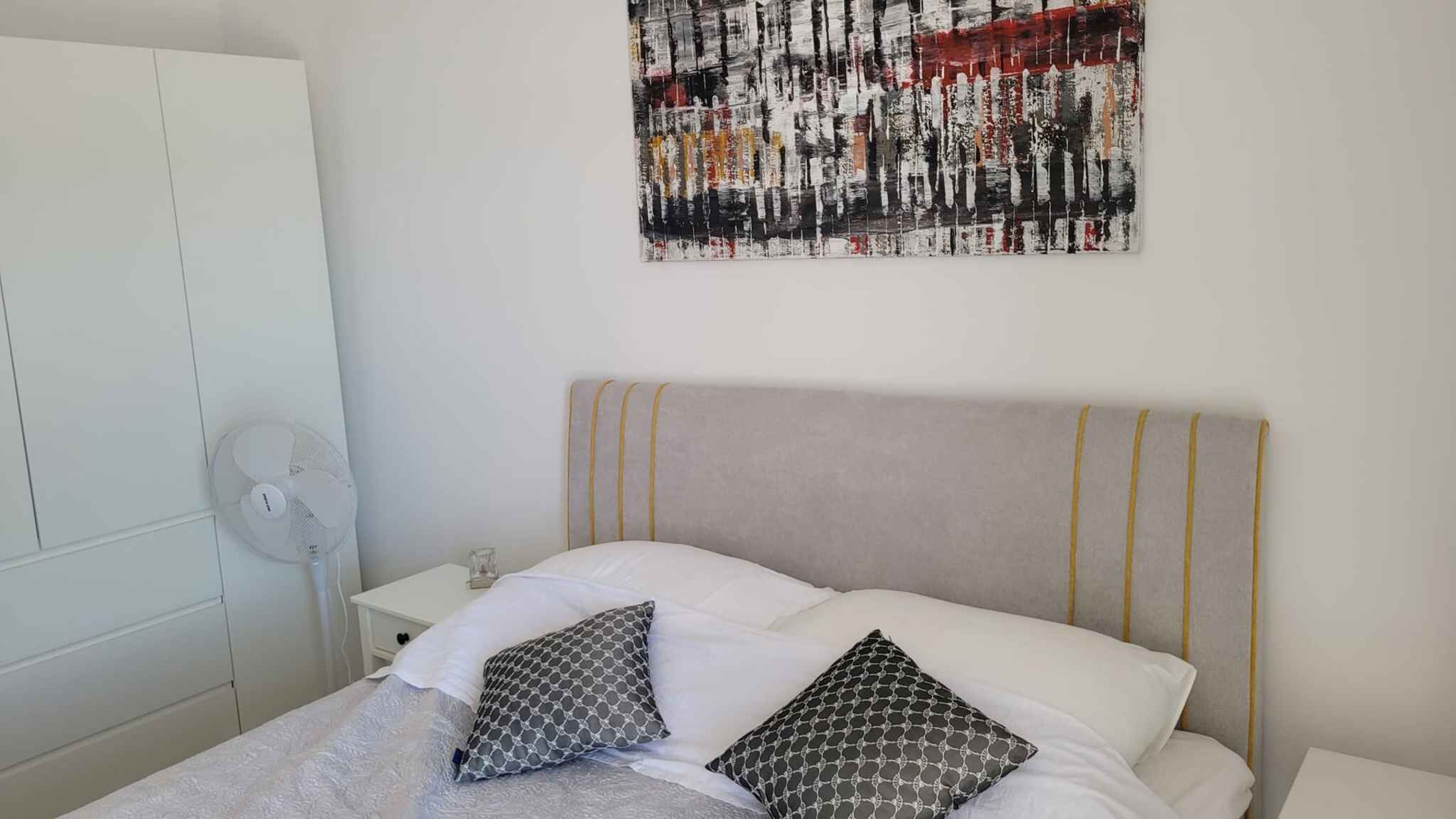A neatly made bed with a grey headboard, two patterned pillows, and a white blanket.