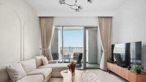 A modern living room with a sofa, coffee table, TV, and a balcony with a view. - 1BR Retreat Near Burj Khalifa (Dubai)