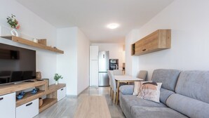 Ett modernt och kompakt vardagsrum med tv, trähyllor, en grå soffa och en matplats.
