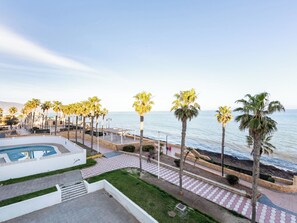 Un complexe hôtelier en bord de mer, doté d’une piscine, de palmiers et d’une promenade le long de la plage.