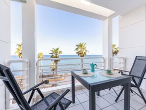 En balkon med et glasbord, stole og udsigt til havet og palmer.