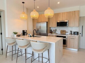 Una cocina moderna con una isla central, electrodomésticos de acero inoxidable e iluminación colgante.