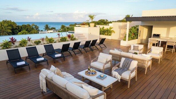 Eine Dachterrasse mit Liegestühlen, einer Sitzecke und einem Tisch mit Blick auf einen Pool und den Ozean.
