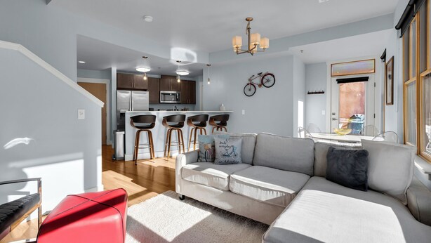 Een moderne woonkamer met een grijze bank, een rode fauteuil en een keuken op de achtergrond.