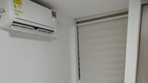 A small, clean room with a bed, a desk with a chair, a window with blinds, and an air conditioning unit. - New apartment well located in a 4 floor brand new with all the comforts. (Barranquilla)