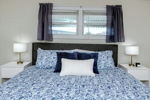 A bed with a blue and white patterned bedspread, two white nightstands with lamps, and a window with curtains. - MINT Julip - Amazing 40+ Community - Newly Updated 2 bed/2 bath single family (Largo)