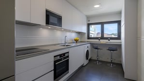 Une cuisine moderne équipée d’un four à micro-ondes, d’un four et d’un lave-linge intégrés, d’une fenêtre offrant une belle vue et de deux tabourets de bar.