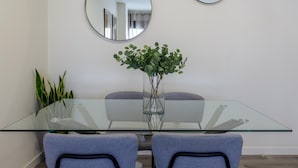 Un espace repas moderne avec une table en verre, deux chaises grises, un vase avec des plantes vertes et deux miroirs ronds accrochés au mur.
