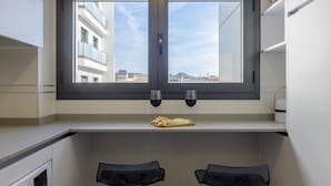 Une cuisine moderne avec une grande fenêtre, deux tabourets de bar et un comptoir sur lequel se trouve un verre de vin rouge.