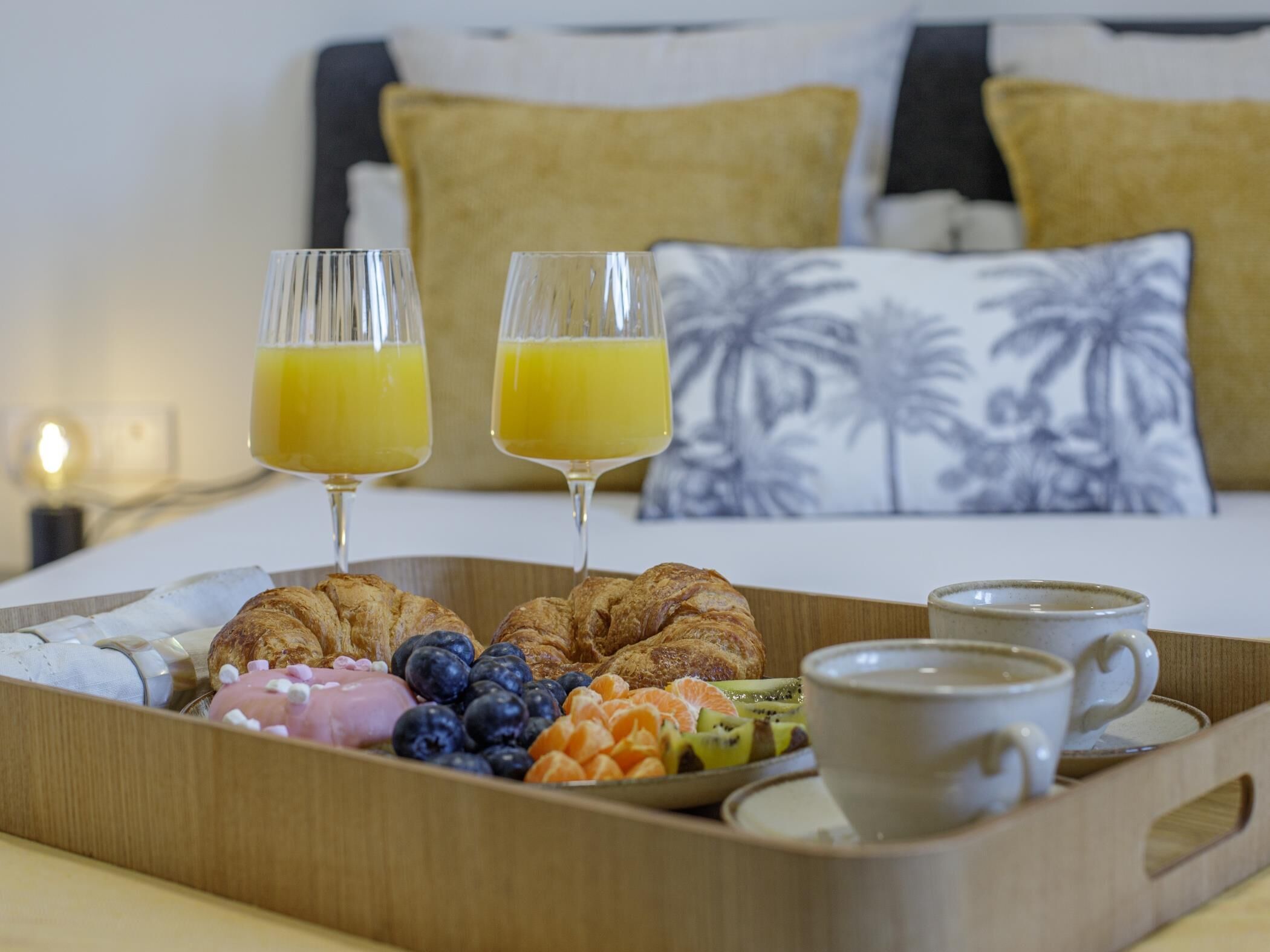 En bakke med morgenmad, blandt andet croissanter, blåbær, kiwi, appelsinskiver og to glas appelsinjuice.