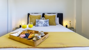 Un lit bien fait, avec un plateau de petit-déjeuner, deux verres de jus d’orange et deux tasses de café posés sur une table de chevet.