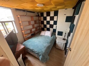 Une petite pièce comprenant un lit, un bureau, une échelle et une fenêtre.