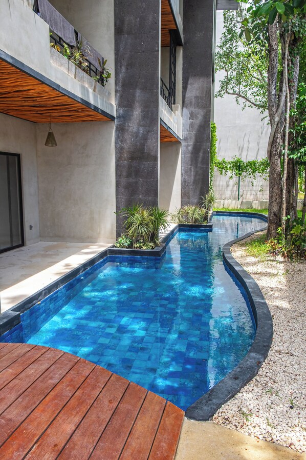 Ein moderner Poolbereich im Freien mit Holzterrasse, umgeben von Betonmauern und Pflanzen.