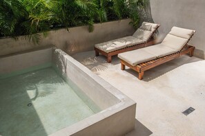 Ein Wellnessbereich mit einem rechteckigen Whirlpool und zwei Holzliegen mit beigen Kissen.