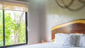 A bedroom with a large bed, a wooden headboard, a bedside table, and a window with a view of trees. - Luxury Penthouse in Tulum with Private Rooftop (Tulum)