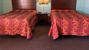 A hotel room with two beds, a nightstand, a lamp, and two framed pictures on the wall.