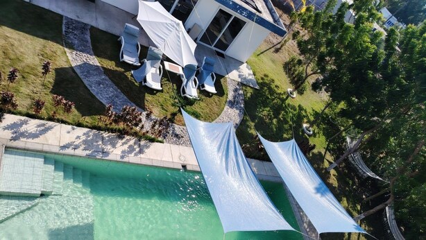 Una piscina en la azotea con agua cristalina, rodeada de un área de descanso con muebles blancos y una sombrilla blanca.