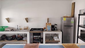 Cocina moderna con estufa a gas, lavaplatos y refrigerador. Hay repisas de madera y una cesta en la encimera.