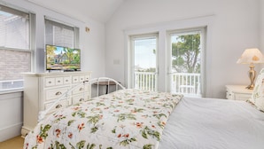 Een slaapkamer met een bed, een dressoir, een televisie en uitzicht op een balkon.