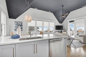 A modern kitchen with a large island, white cabinetry, and a ceiling fan. - High dunes of Bramble Reach cottage with ocean views (Bald Head Island)