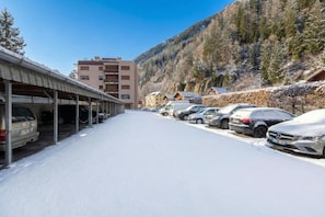 Ein verschneiter Parkplatz mit dort geparkten Autos, neben einem Gebäude mit einem überdachten Gang.