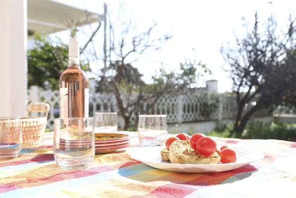 Une table recouverte d’une nappe colorée, une bouteille de vin, des verres, des assiettes et une assiette avec un sandwich et des tomates.