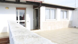 Un immeuble résidentiel doté d’un patio carrelé, d’une porte-fenêtre coulissante et d’une fenêtre avec des rideaux.