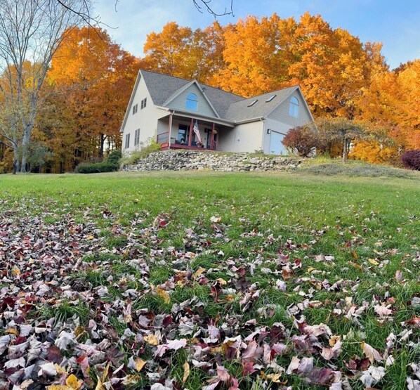 Une maison avec des fondations en pierre, un porche et une pelouse jonchée de feuilles mortes.