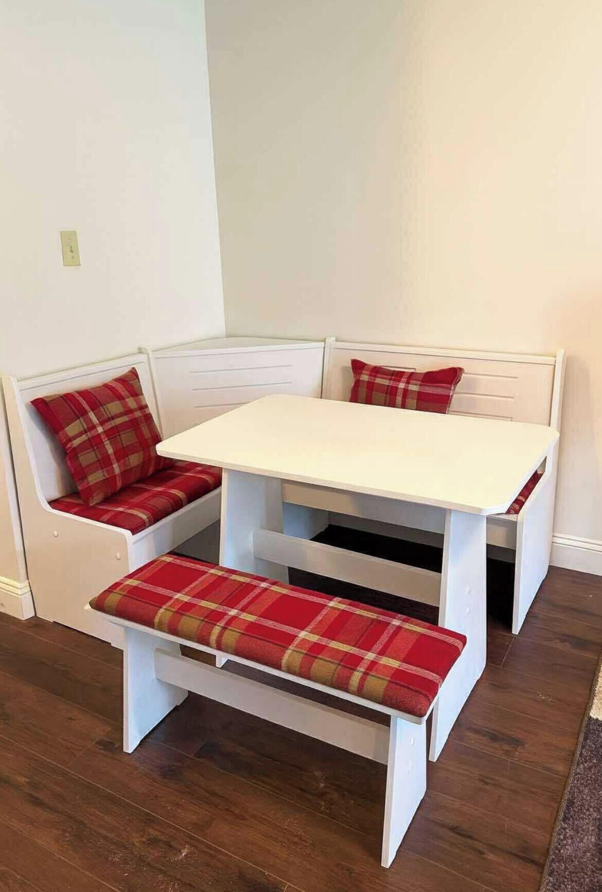 A corner seating area with a white table and bench, featuring plaid cushions.