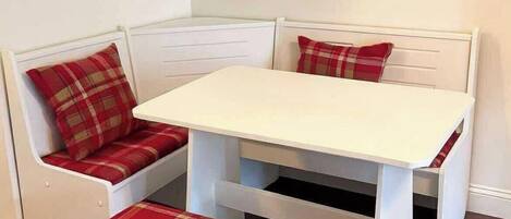 A corner seating area with a white table and bench, featuring plaid cushions.