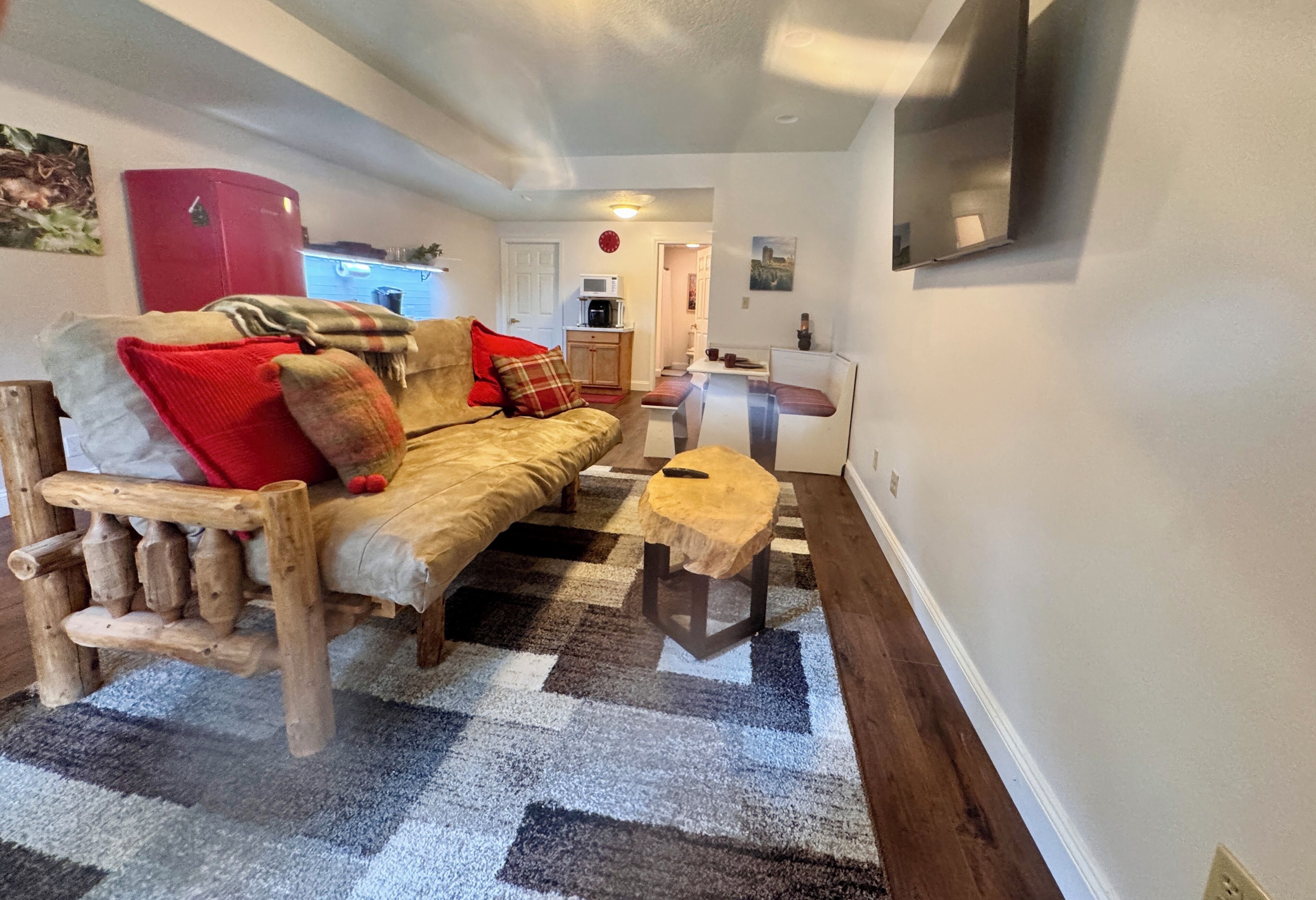 Un salon chaleureux avec un canapé en bois, un petit tabouret et un tapis à motifs.