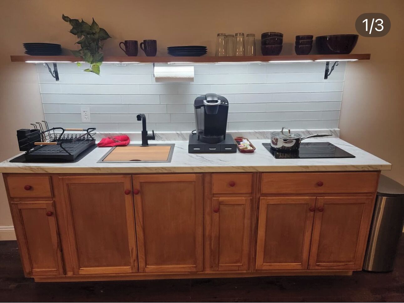 Une cuisine avec des meubles de rangement en bois, un plan de travail, une machine à café et une plante suspendue.