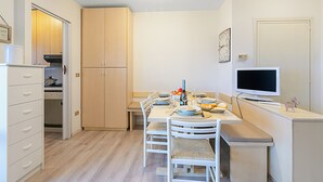 Een praktische keuken met witte kastjes, een eettafel gedekt voor vier personen, een televisie en een kleine koelkast.